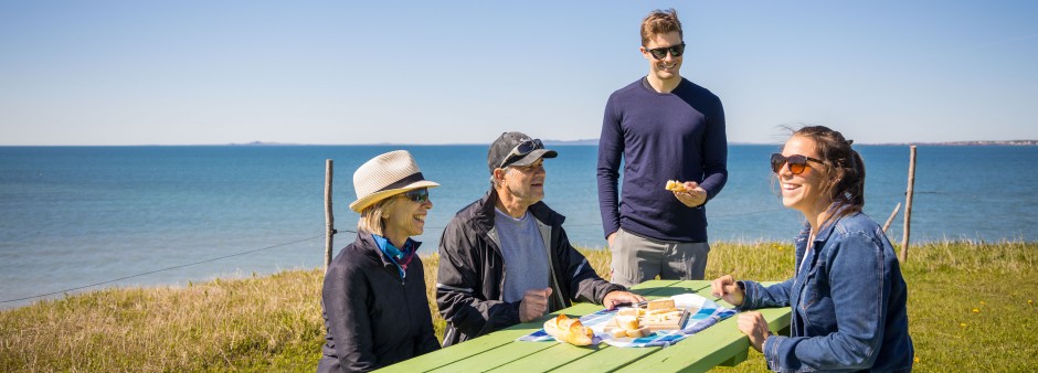 Four people eating lunch on a picnic table by a beautiful sunny day next to the blue sea