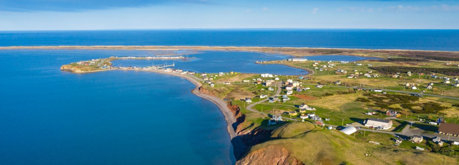 Vue aérienne des Îles de la Madeleine montrant les falaises rouges, les maisons colorées et le littoral du golfe du Saint-Laurent.
