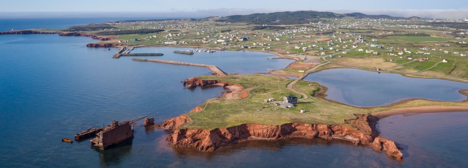  Vue aérienne de l'île du Cap-aux-Meules aux Îles de la Madeleine, avec les falaises rouges, le littoral et l'épave d'une gabarre échouée en 1988 lors d'une tempête.